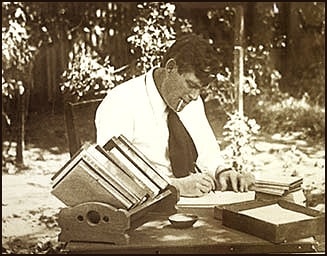 Jack london outside in yard writing on paper at desk by hand. 