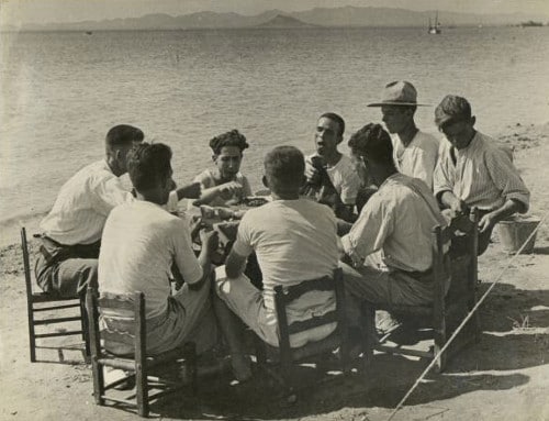 vintage men eating around dinner table on beach ocean