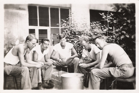 White tees vintage men sitting around and cutting something with a knife's. 