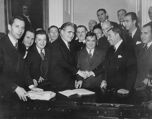 Vintage men suits shaking hands big group around behind them.