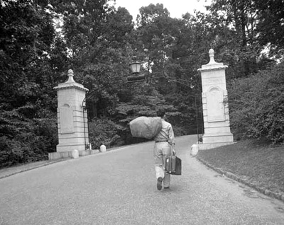 Vintage man walking through gate with carrying bag and suit case. 