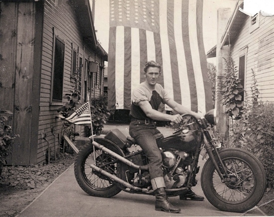 Vintage man sitting on motorcycle in front of american flag. 