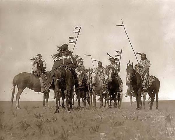 Vintage men riding on horses with flag poles. 