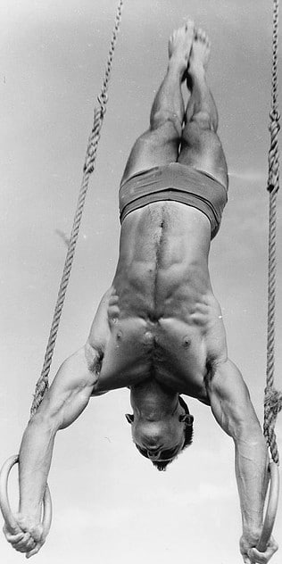 Vintage gymnast athlete hanging on gymnastic rings with both hands.