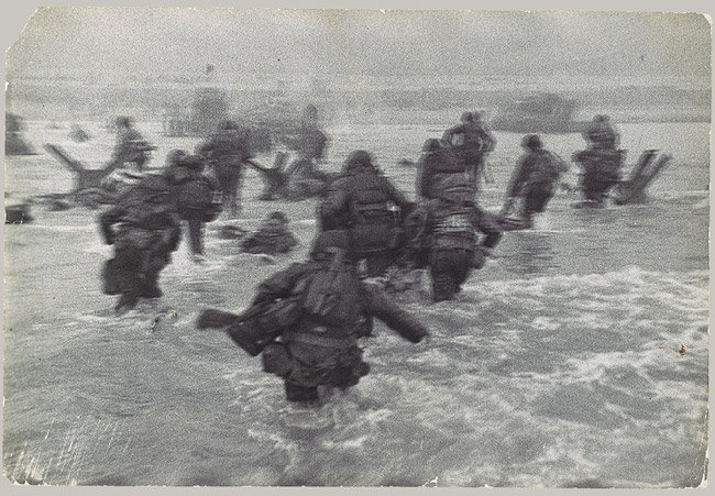 D-day Normandy photo men storming beaches through shallow seawater.