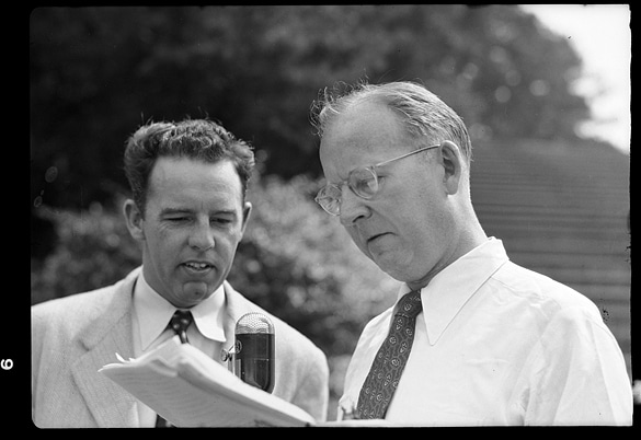 Vintage businessmen looking at papers talking while standing up.