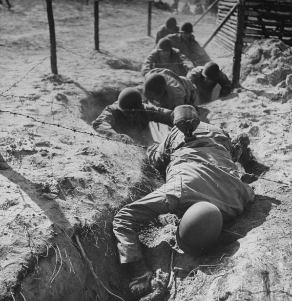 Vintage soldiers crawling through trench boot camp under barbed wire.