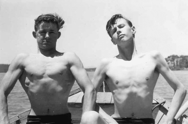 Two vintage young men puffing chests flexing muscles on boat.