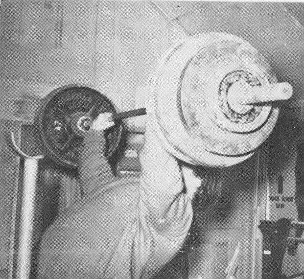 Vintage man lifting barbell with heavy weights above head.