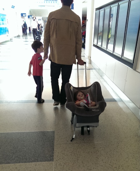man walking through airport wheeling baby in carseat