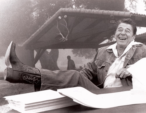 Ronald Reagan wearing cowboy boots feet up on table.