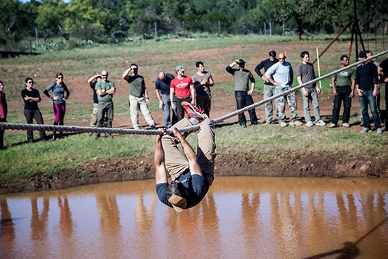 atomic athlete vanguard man hanging from rope over mud pit