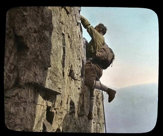 Vintage man scaling climbing rock cliff wall.