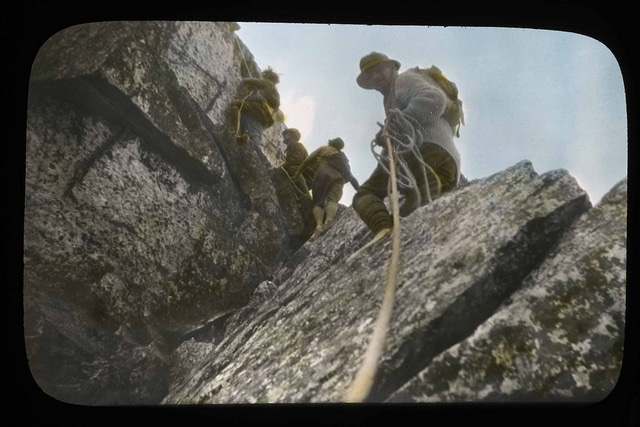 Vintage rock climber looking up cliff wall towards other climbers.