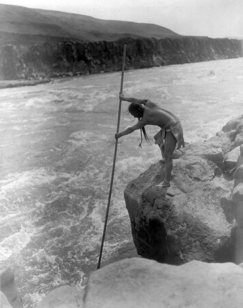 Vintage native american man fishing in large river with spear.