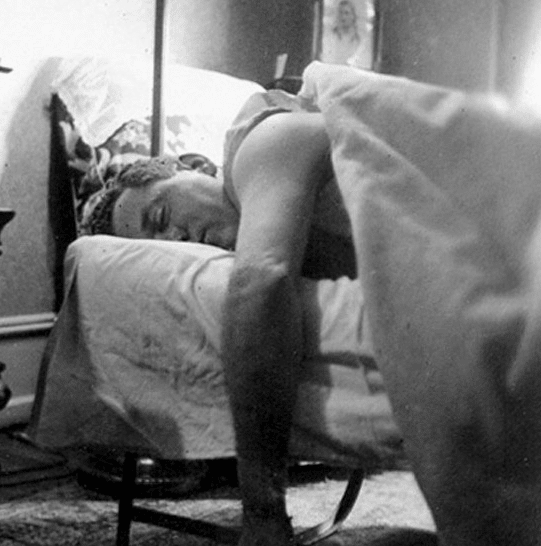 Vintage man sleeping on cot arm over side. 