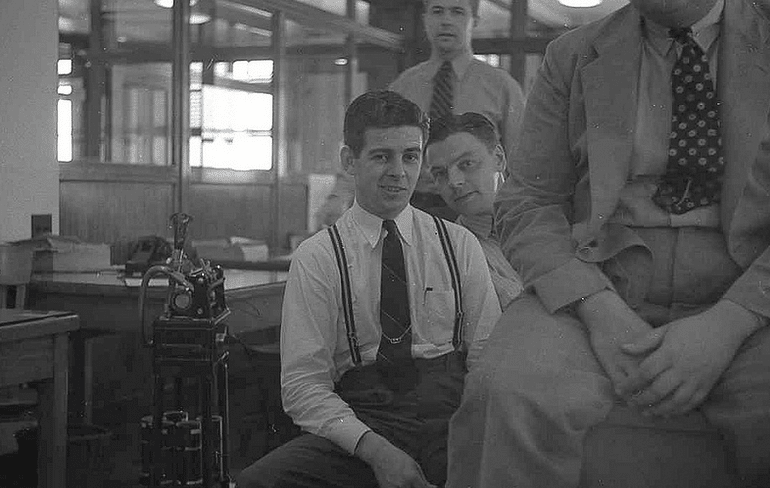 Young workers in office sitting on desks. 