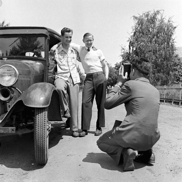 Vintage friends posing for picture in front of car. 