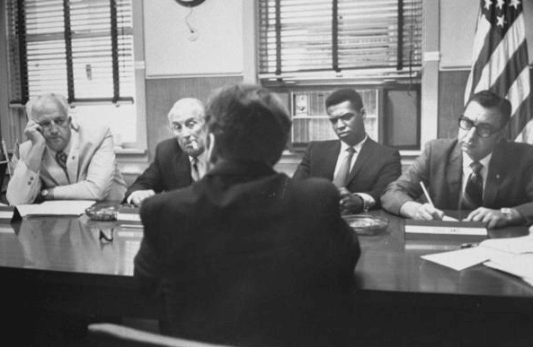 Vintage men being interviewed at conference table. 