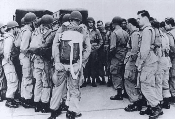 Vintage paratroopers in group wearing backpacks being briefed.