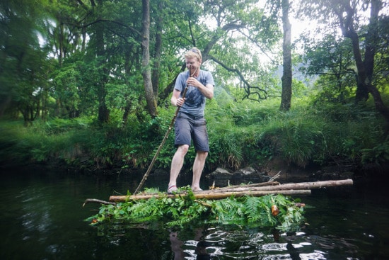 man on log raft floating in river