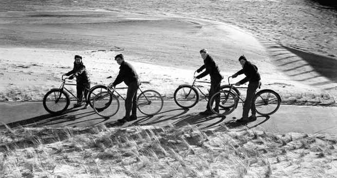 Vintage young men riding bikes beach winter.