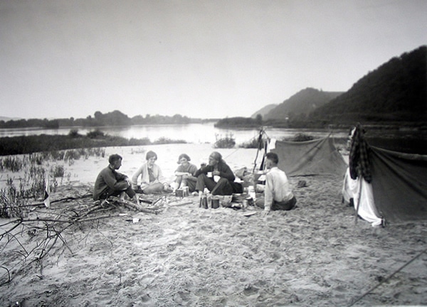 Vintage group of people camping on sand bank river.