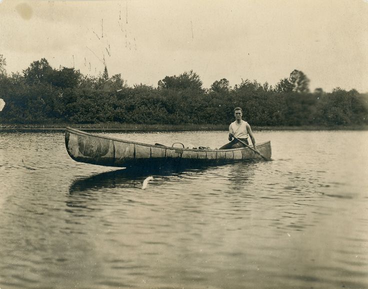 Vintage man in canoe paddling on lake.