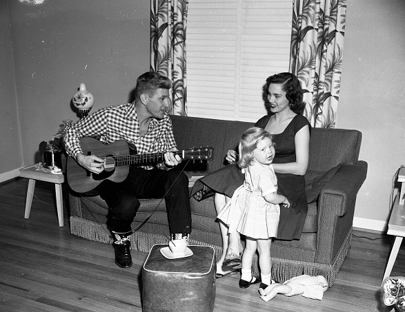 Vintage man playing guitar for wife daughter in house.