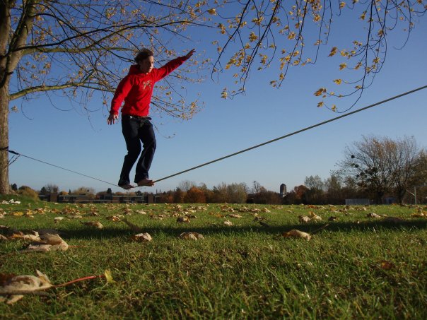 Young man slacklining between trees open grass field.