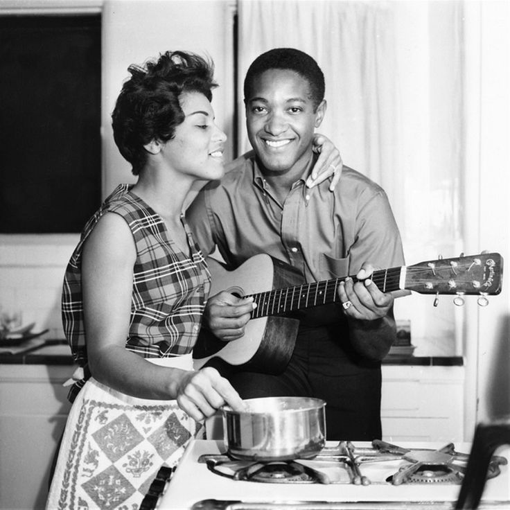 Vintage couple playing guitar while cooking in kitchen.