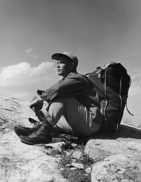 A mountain climber sitting on rock with bag.