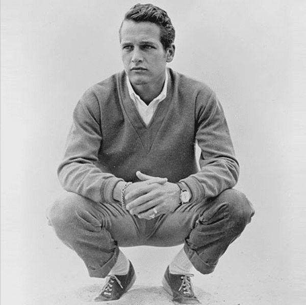 Paul newman sitting on ground with khakis sweater. 