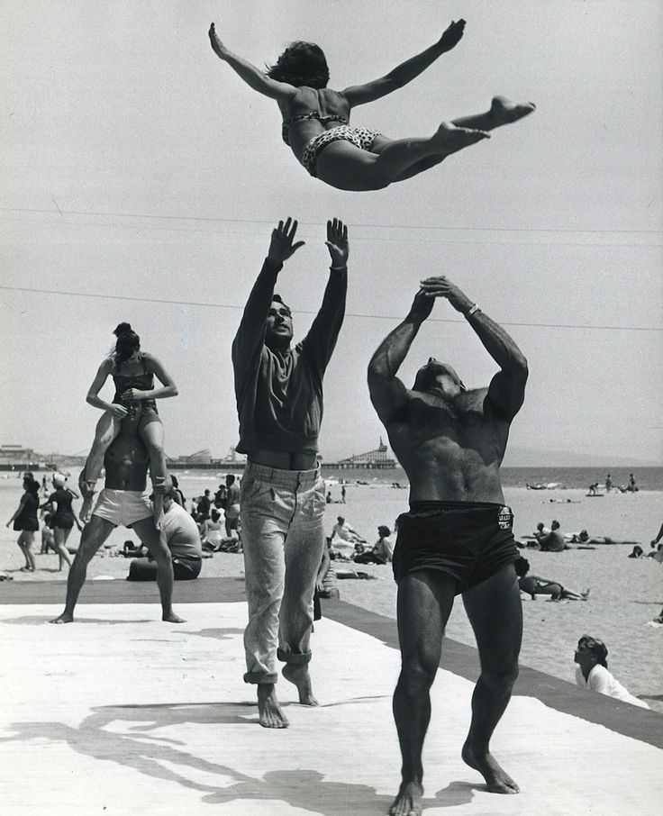 Vintage men on beach throwing woman into air.