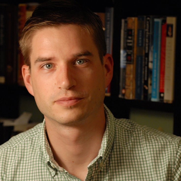 Cal newport author sitting for a picture with bookshelves behind him.