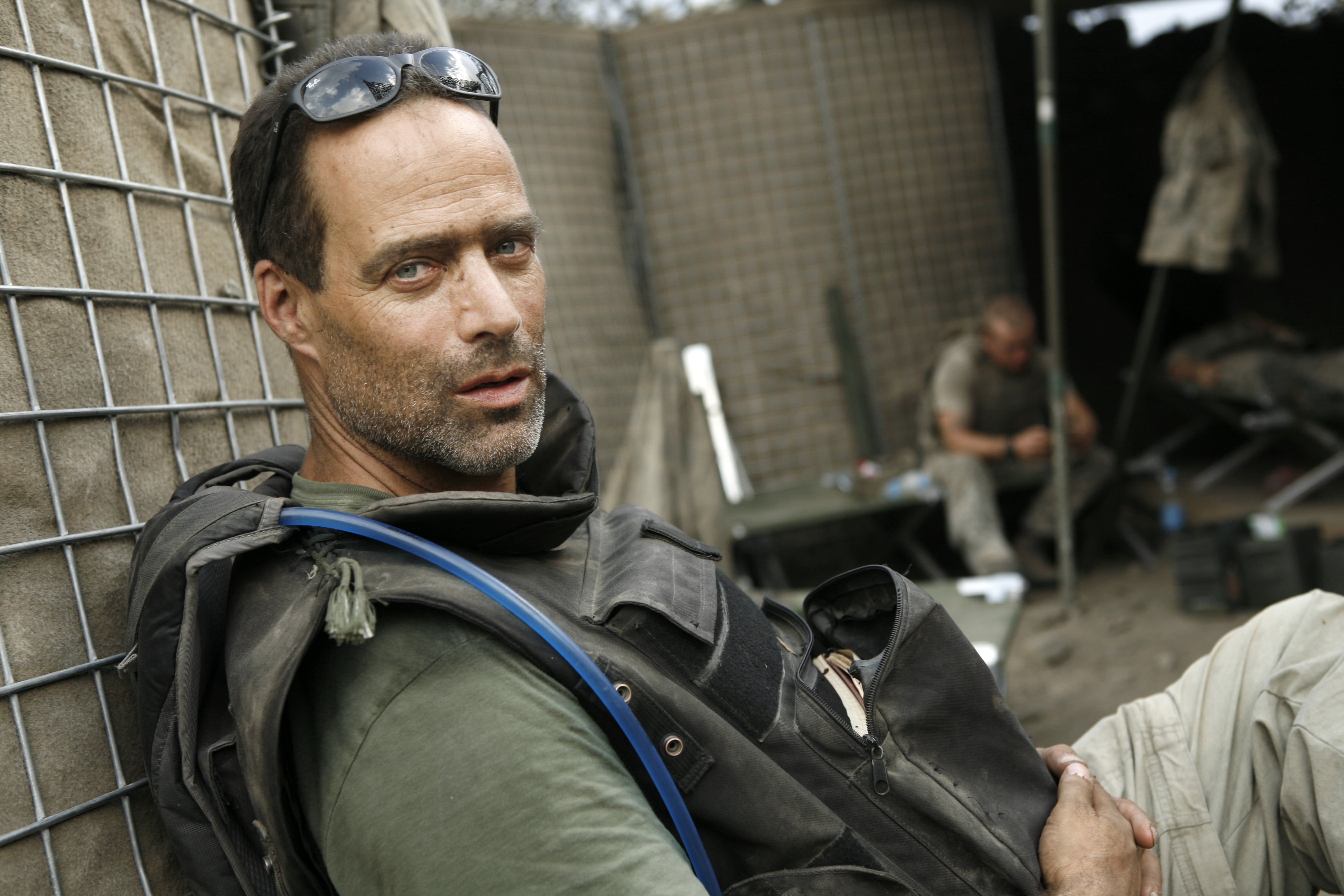 Sebastian junger in military camp wearing camelbak and glasses on forehead.