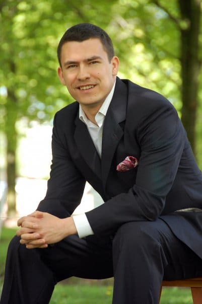 A man in a suit sitting on a bench in a park.