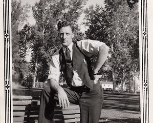 Man in vintage attire exuding manly confidence while sitting on a park bench.