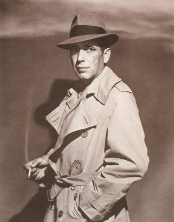 Humphrey bogart wearing fedora and trench coat cigarette in hand.