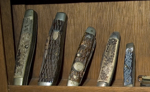 A row of pocket knives on a wooden shelf.
