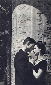 A man and a woman kissing in front of a column.