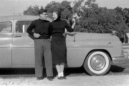 Vintage couple standing in front of car.