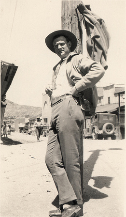 A man in a cowboy hat, displaying vital characteristics, leans against a pole.