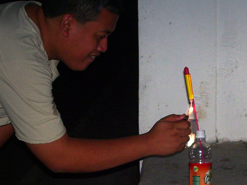 man lighting bottle rocket firework