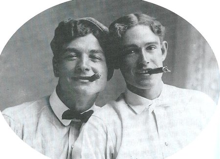 Two men are posing for a picture with a cigar in their mouth, capturing a nostalgic moment of their long-standing friendship.