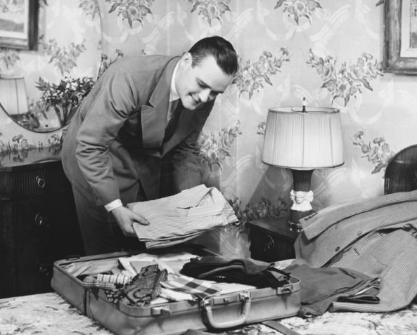 A traveling man unpacking a bag on a bed.