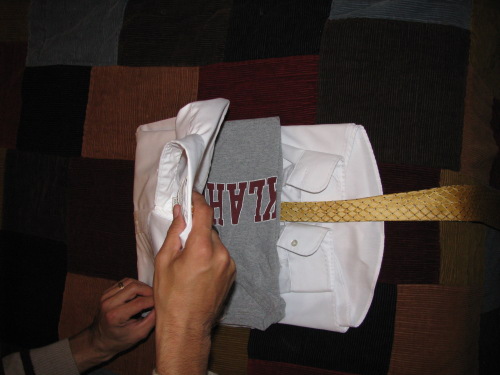 A man folding t shirt and tie in shirt.