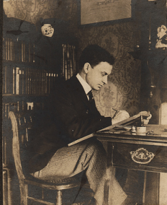 Vintage man studying at desk rack of books in back.