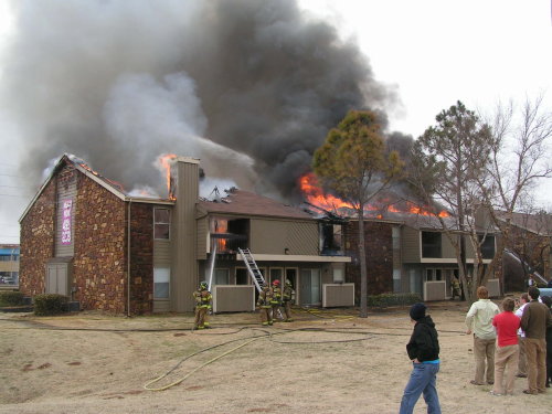 Firefighters working on burning house and crowd of people looking.