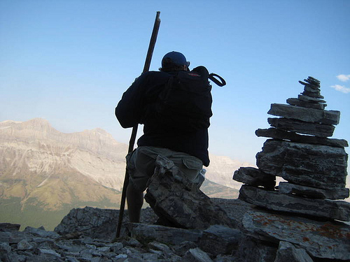 Hiker on top of mountain sitting on a cairn.